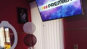 A room with a television displaying the word "PREMIER," a white chair, a small table with a vase, and a red wall. - Gran Copacabana Hostal (El Alto)