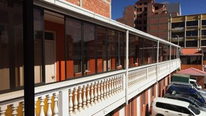 A multi-story building with a balcony, a white car parked in front, and a brick building in the background. - Gran Copacabana Hostal (El Alto)
