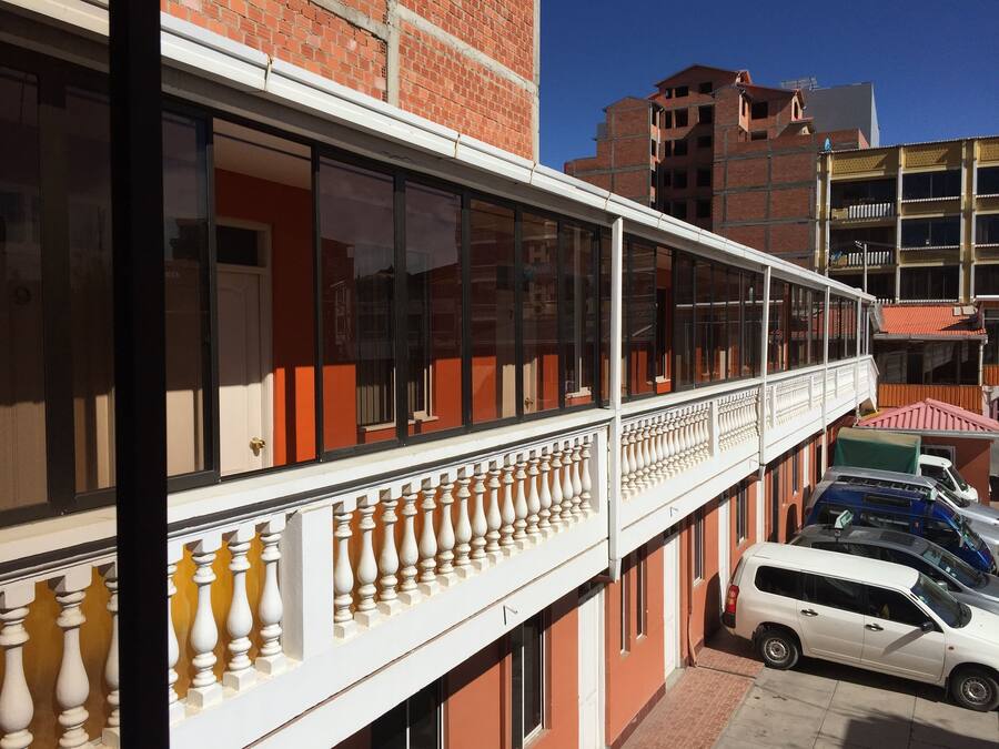 Un edifici de diverses plantes amb un balcó, un cotxe blanc estacionat al davant i un edifici de maó al fons.