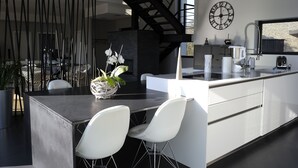 Een moderne keuken met een centraal eiland, witte stoelen, een klok en een trap.