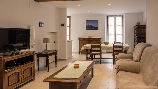 Una sala de estar con televisor, muebles de madera, un comedor con mesa y sillas, y un sofá.