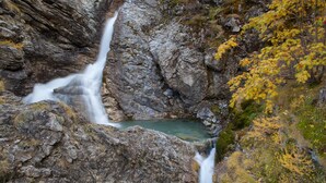 Una cascada se precipita por un risco rocoso rodeado de follaje otoñal.
