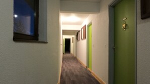 A hallway with wooden flooring, green doors, and framed pictures on the walls.