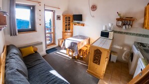 A cozy room with a sofa, a dining table, a wooden cabinet, a television, and a kitchen area with a washing machine.