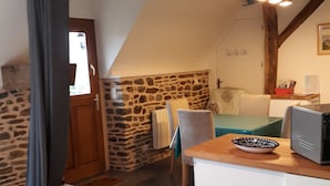 Una habitación acogedora con pared de piedra, viga de techo de madera, una mesita con un cuenco, una silla y una cama con cubierta blanca.