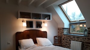 Un dormitorio con techo inclinado, cama de madera, dos lámparas de noche, pared de piedra y tragaluz.