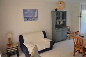 A living room with a sofa, a small table with a lamp, a cabinet, and a dining table with chairs.