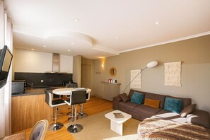 A modern living room with a sofa, coffee table, and a dining area with chairs. - 2-Bedroom Apartment with Parking - Maison de l'Octroi (Chartres)