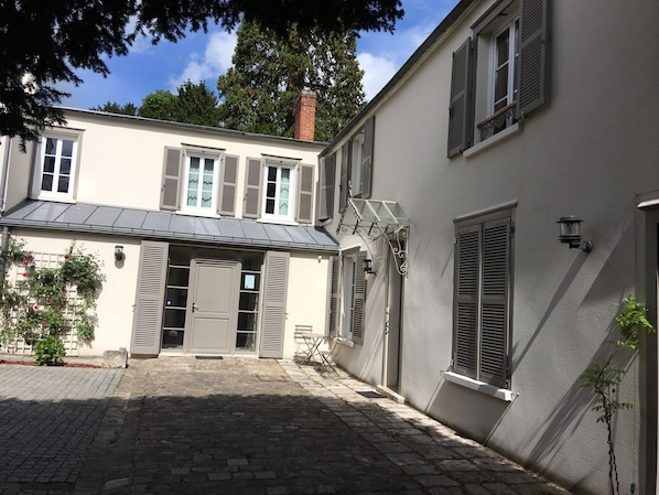 Un bâtiment à deux étages doté d’une cour pavée, d’une entrée couverte et d’un petit espace extérieur aménagé pour s’asseoir.
