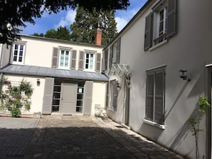 Un bâtiment à deux étages doté d’une cour pavée, d’une entrée couverte et d’un petit espace extérieur aménagé pour s’asseoir.