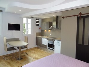 A compact kitchen with a dining area, a built-in oven, and a television mounted on the wall. - 2-Bedroom Apartment with Parking - Maison de l'Octroi (Chartres)
