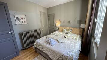 A bedroom with a bed, a radiator, a door, and a wall with a plant and a lamp.