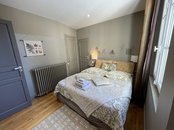A bedroom with a bed, a radiator, a door, and a wall with a plant and a lamp. - 2-Bedroom Apartment with Parking - Maison de l'Octroi (Chartres)