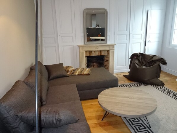 Una sala de estar con un sofá modular, una mesa redonda de centro, una chimenea y un espejo encima.