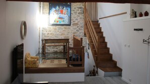 Una habitación con escalera de madera, un banco, una mesita y un cuadro en la pared.