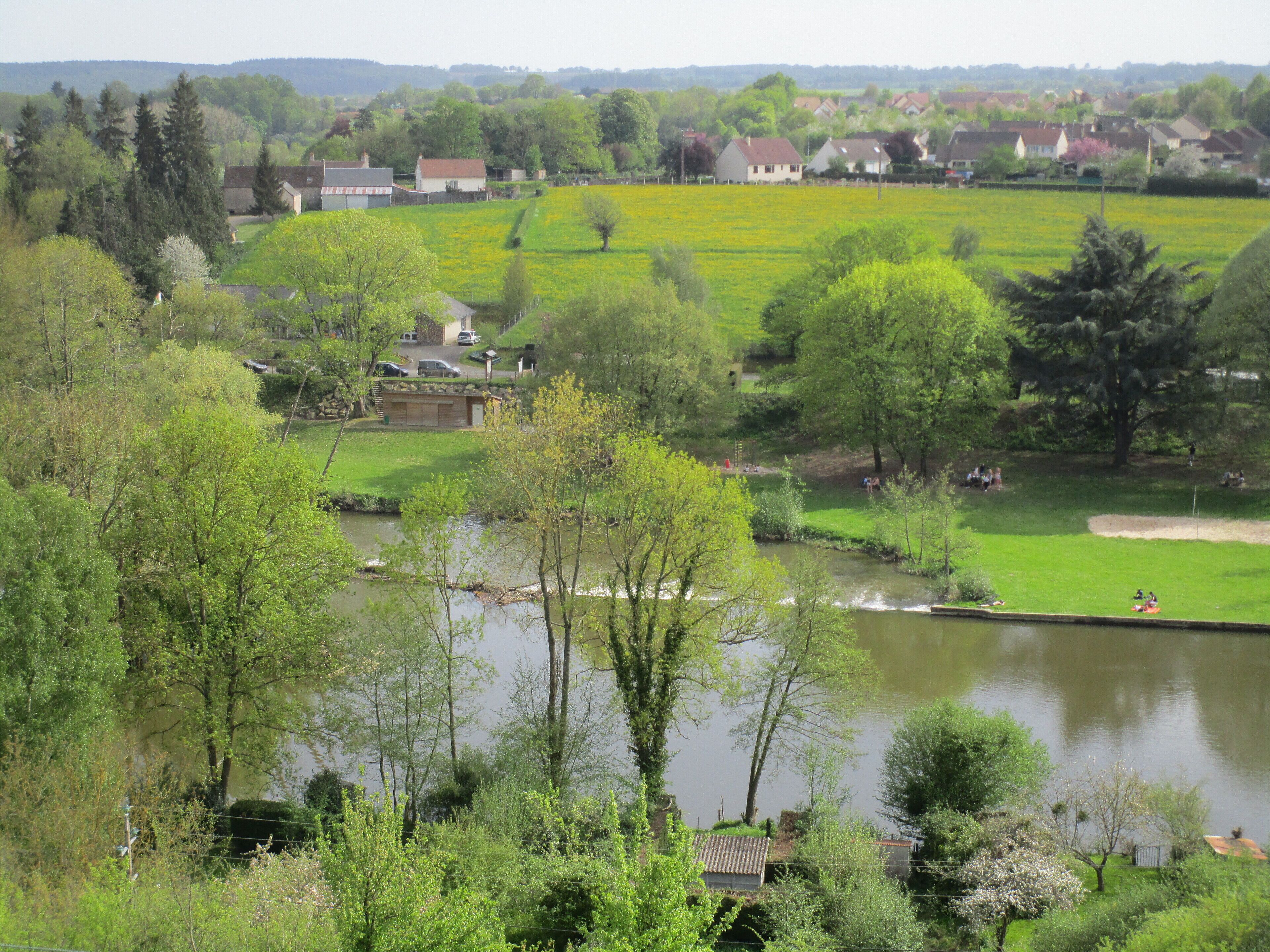 Vista de la orilla de un río con casas, vegetación y un pequeño embarcadero.