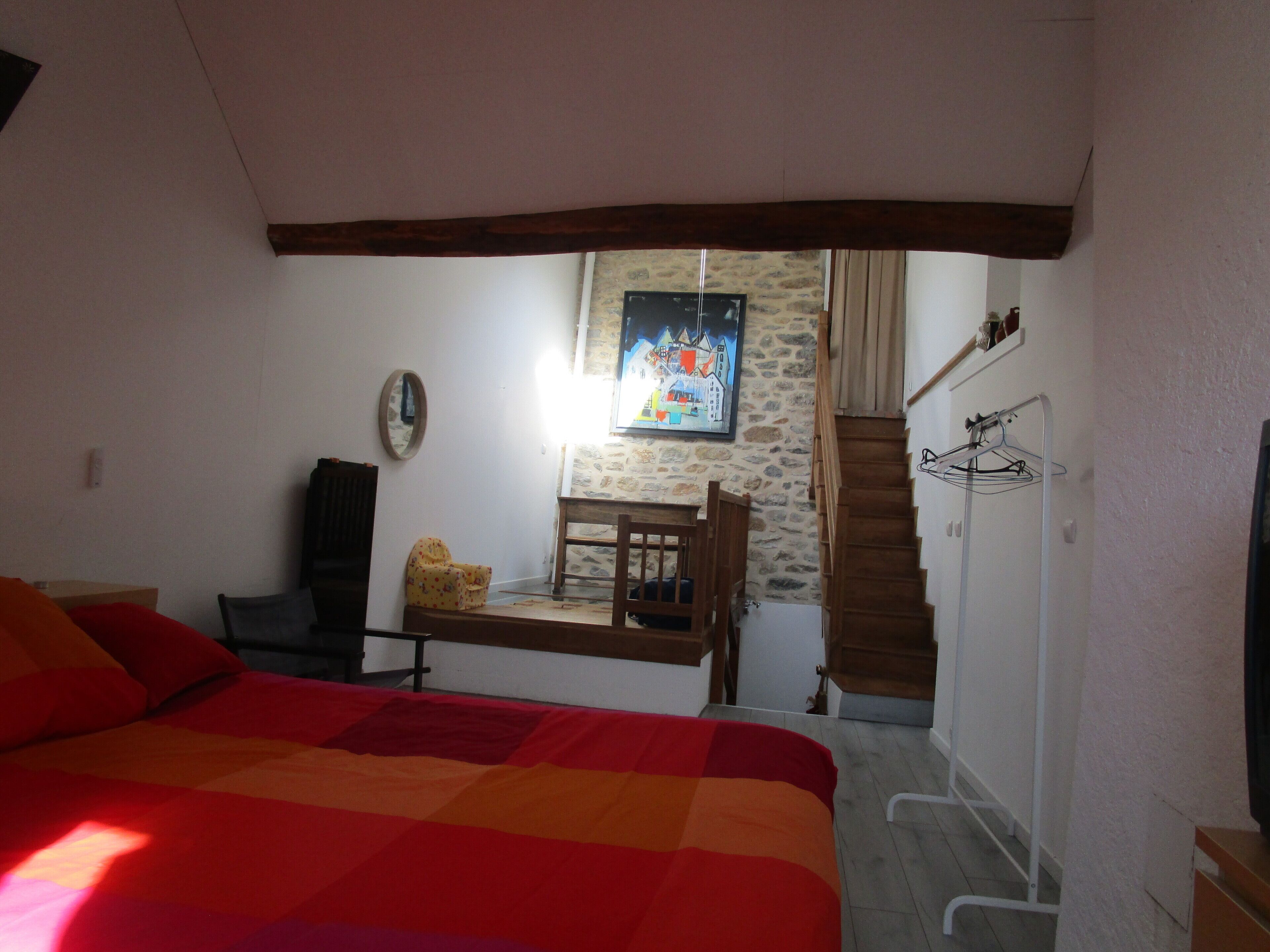 Une chambre à coucher comprenant un lit, un bureau, une chaise, un miroir, un tableau, un escalier et une armoire.
