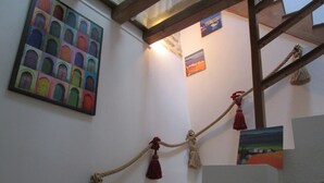 Una cuerda con borlas colgando de una viga de madera, un colorido cuadro de arcos y un pequeño cuadro de paisaje en la pared.