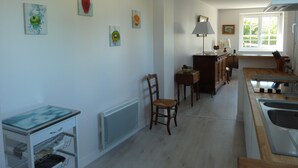 Une cuisine avec un plan de travail en bois, un évier et une fenêtre. On y trouve des étagères fixées au mur et une chaise.