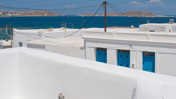 Edifici blanc amb portes blaves, una banyera blanca i vista al mar.