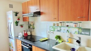 Una cucina con mobili in legno, forno integrato, piano cottura, lavello e un piano di lavoro con diversi oggetti, tra cui un estrattore di succo, un frullatore e dei vasetti su uno scaffale etichettato 'NATURE'.
