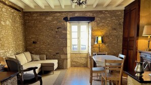 A cozy room with a stone wall, a wooden dining table with chairs, a sofa, and a small window. - Gabarier's house in the historic heart of the medieval village of La Roque Gageac (La Roque-Gageac)