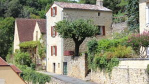 A stone building with a tiled roof, surrounded by greenery and other buildings. - Gabarier's house in the historic heart of the medieval village of La Roque Gageac (La Roque-Gageac)