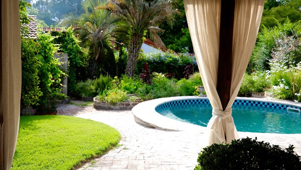 A pool area with a curved edge, surrounded by lush greenery and a stone pathway.