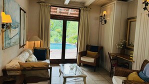 A cozy living room with a sofa, armchairs, a glass coffee table, and a view of a swimming pool through a glass door.
