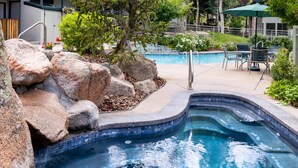 A swimming pool with a curved edge, surrounded by large rocks and greenery.