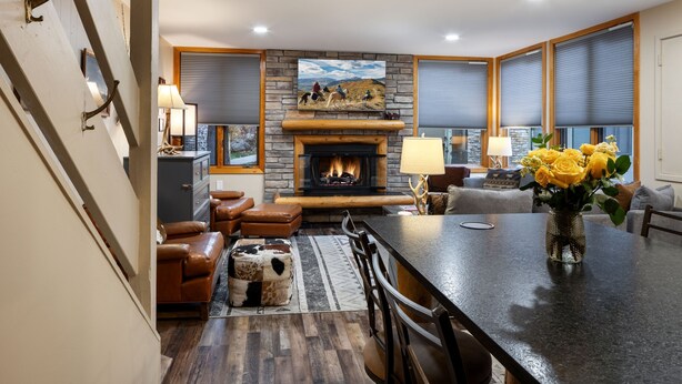 A modern living room with a stone fireplace, leather furniture, and large windows with blinds.