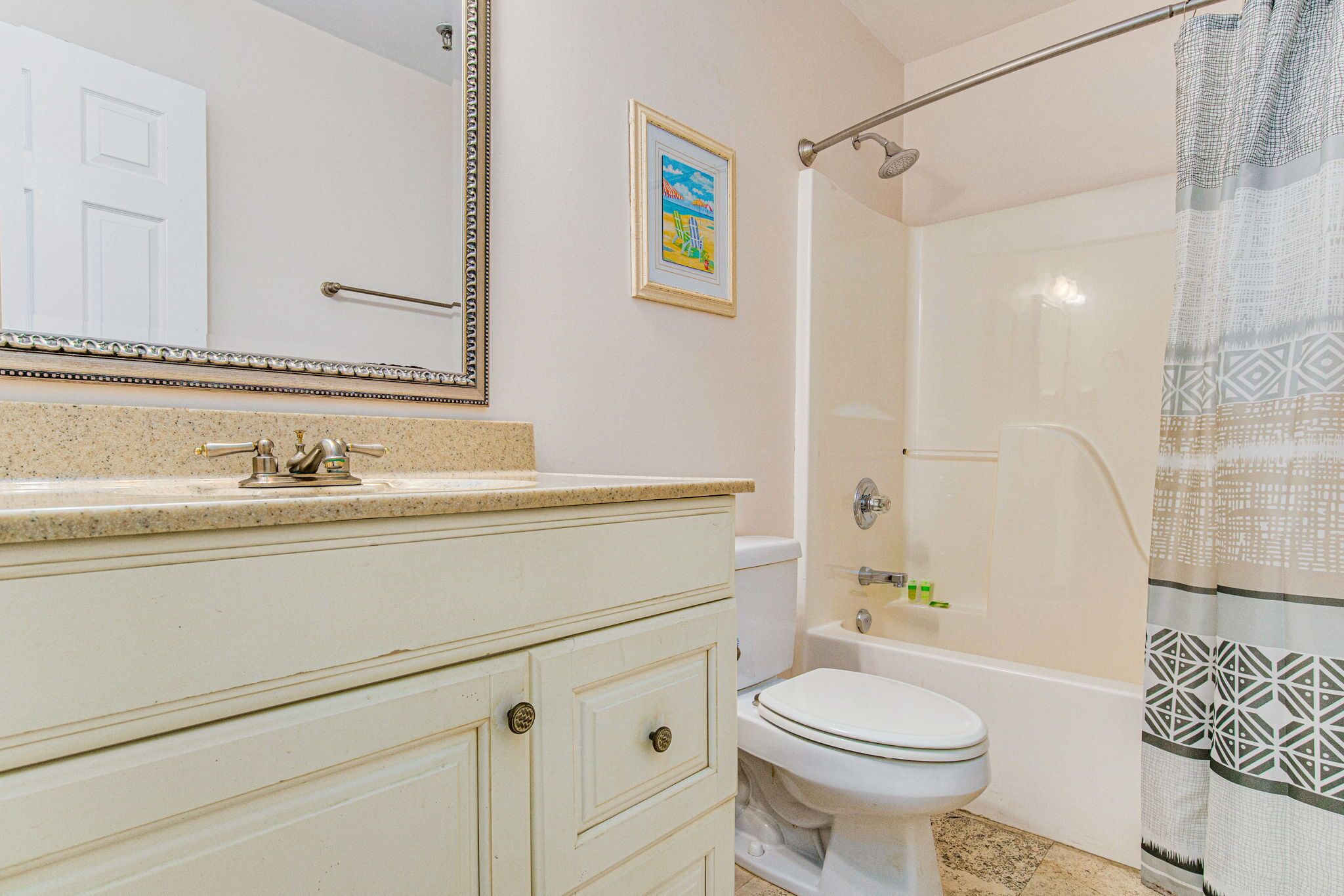 A bathroom with a white sink, toilet, and bathtub. There is a framed picture on the wall and a shower curtain with a geometric pattern.