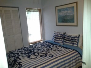 A bedroom with a bed, a window with blinds, a door, and a framed picture on the wall. - Location, location, location!  Ocean view!  Swimming & surfing within steps! (Kihei)