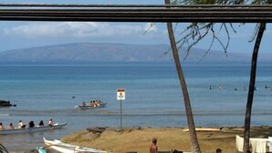 A beach with a sign, palm trees, and a boat in the water.