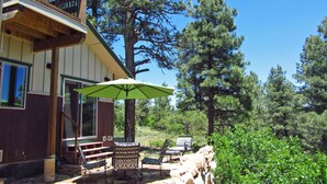A wooden house with a balcony, outdoor seating, and a large umbrella. - New-ish 3 BR house on canyon ridge/Borders Forest/31 windows- 3 miles from town (Pagosa Springs)