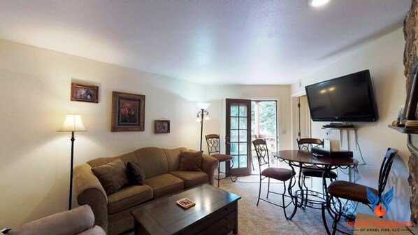A living room with a sofa, coffee table, TV, and dining area with chairs and a table.