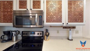 A kitchen with stainless steel appliances, decorative copper backsplash, and a coffee maker.
