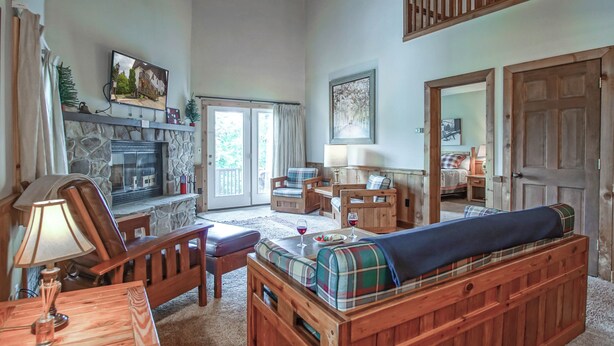 A cozy living room with a stone fireplace, wooden furniture, and a large window with curtains. - Whistlepunk #12:  4 Bedroom, 3 Bath:  Slope Side, Wood Fireplace. (Snowshoe)