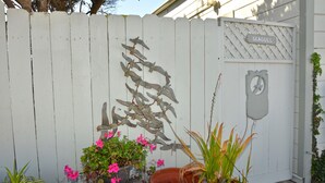 A white wooden fence with a sign reading "SEAGULL" and a coat of arms. There are potted plants and flowers in front of the fence. - Magnificent Ocean views! On Oceano sandy beach with fire pit  (Oceano,)