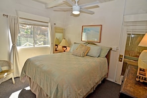 A bedroom with a bed, a ceiling fan, a window with curtains, a chair, and a lamp.