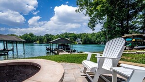 A waterfront patio with Adirondack chairs, a fire pit, and a dock extending into the water. - USAF VETERAN OWNED - DEEP WATER, HUGE HOME, Fire Pit, WiFi, Kayaks/SUP's! (Huddleston)