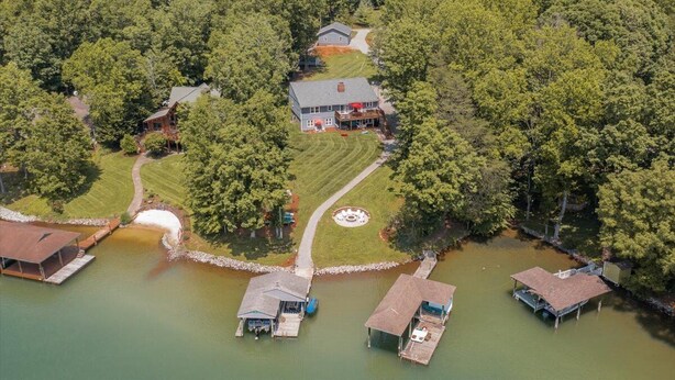 An aerial view of a lakeside property with a main house, docked boats, and a well-maintained lawn. - USAF VETERAN OWNED - DEEP WATER, HUGE HOME, Fire Pit, WiFi, Kayaks/SUP's! (Huddleston)