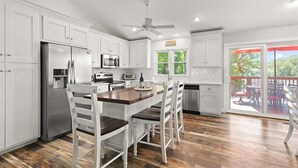 A modern kitchen with white cabinetry, a stainless steel refrigerator, a built-in microwave, and a wooden island with bar stools. - USAF VETERAN OWNED - DEEP WATER, HUGE HOME, Fire Pit, WiFi, Kayaks/SUP's! (Huddleston)