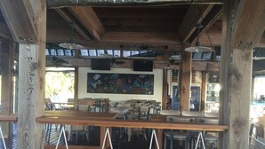 A wooden deck with a bar area, multiple tables and chairs, and a large wall mural.
