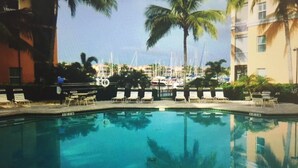 A swimming pool with lounge chairs and palm trees, surrounded by a building with balconies.