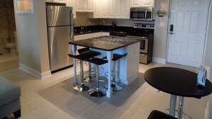 A modern kitchen with white cabinets, stainless steel appliances, a central island with bar stools, and a small dining table.