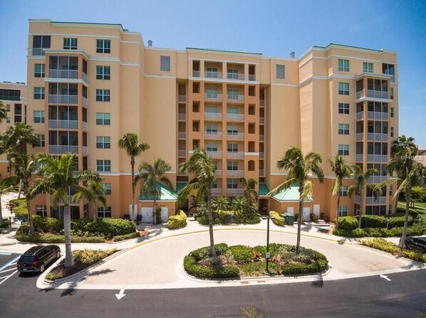 A multi-story hotel with a central courtyard, palm trees, and a clear sky.