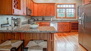 Una cocina con armarios de madera, encimeras de granito, un refrigerador y una ventana.