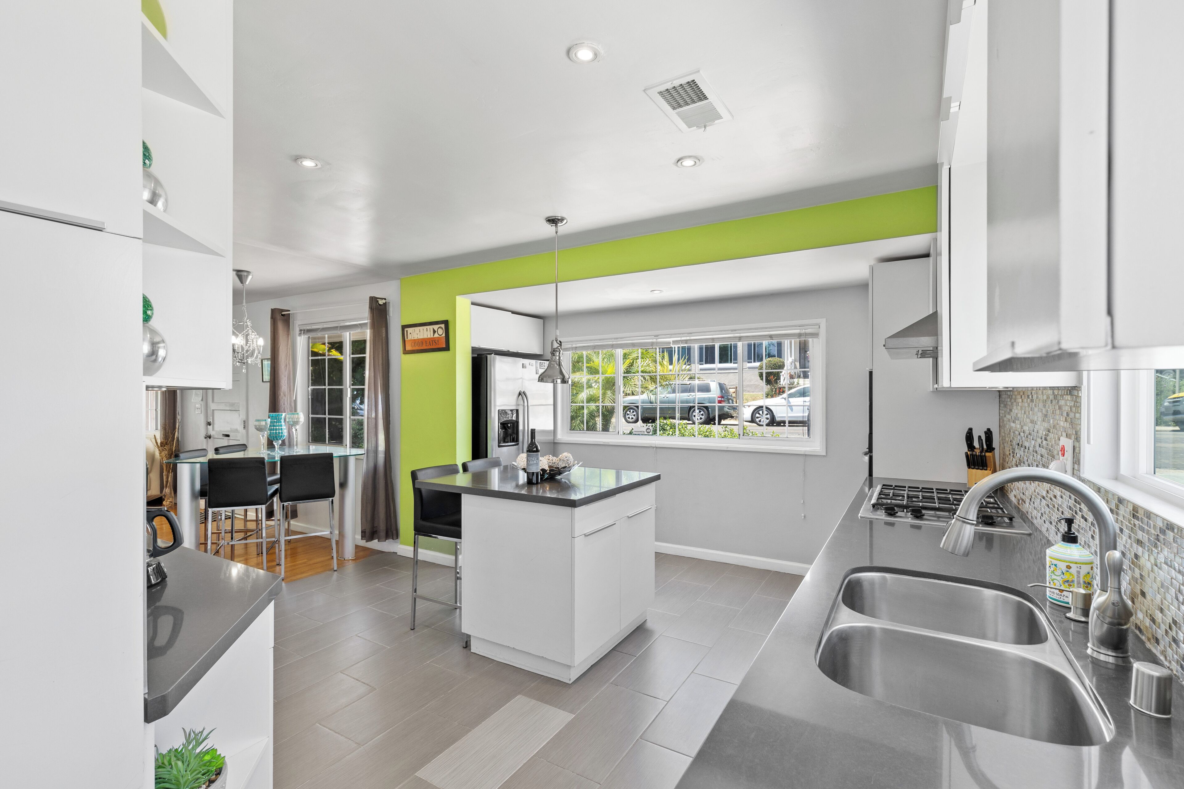 A modern kitchen with a central island, a dining area with chairs, a window with a view of the outside, and a built-in oven.
