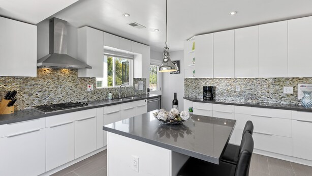 Una cocina moderna con armarios blancos, una isla central y un salpicadero con mosaicos.